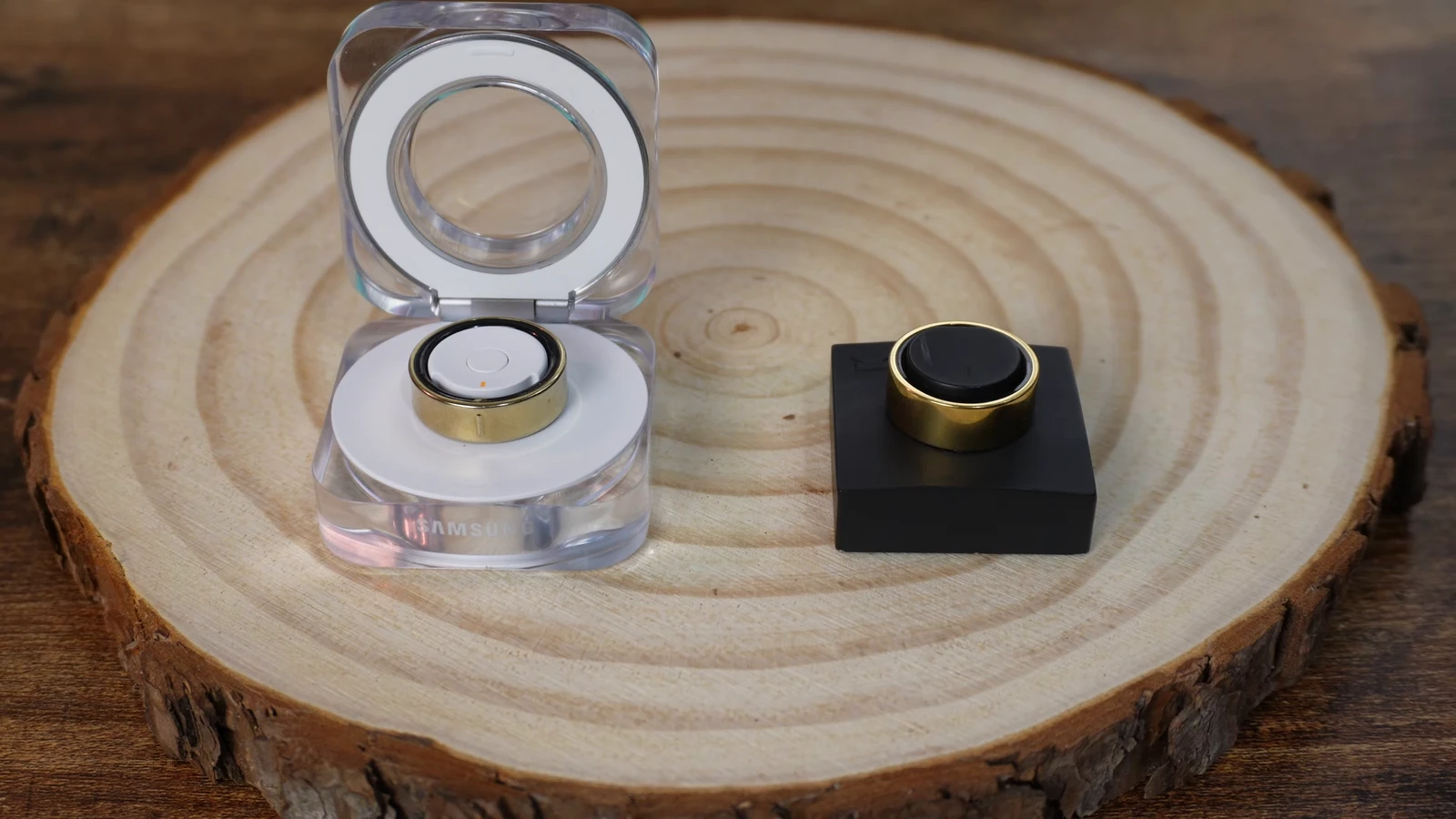Samsung Galaxy Ring charging case open with the ring inside, beside the Ultrahuman Ring AIR sitting on its charging dock